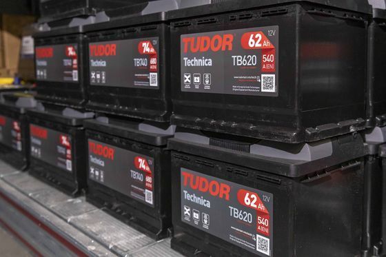 Batterie per auto nere impilate sugli scaffali di un negozio, con etichette rosse e bianche.