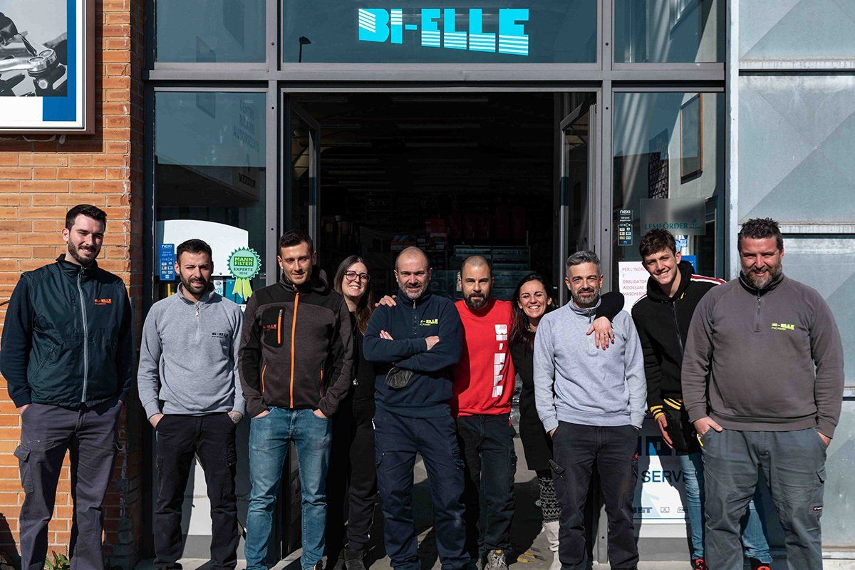 Un gruppo di persone in piedi davanti a una vetrina con un'insegna blu, in posa per una foto.