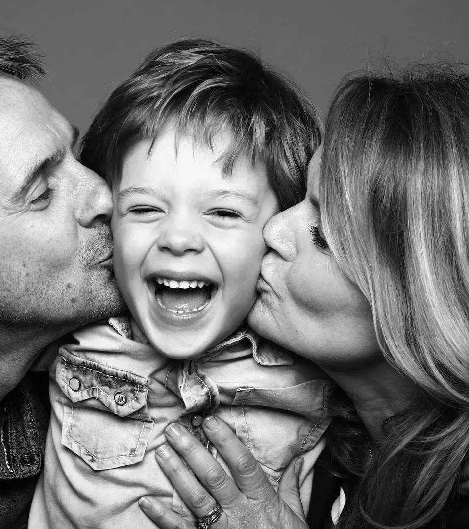 Parents kissing their laughing young son on the cheeks, family dentistry near Southampton
