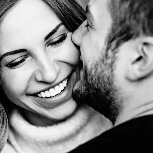 Woman smiling with white teeth as her partner kisses her cheek, cosmetic dentistry near Southampton
