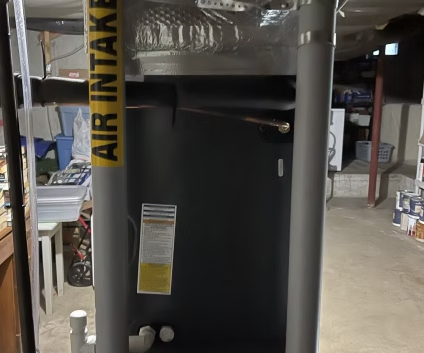 Black air handler unit in a basement, with a warning label and yellow “AIR HANDL” duct strap.