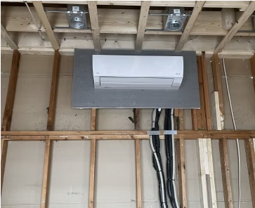 Partially installed white wall-mounted mini-split AC on an exposed stud wall under ceiling joists