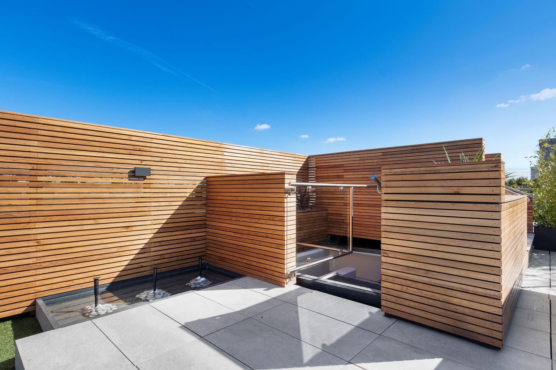 Wooden structure with slatted walls on a rooftop patio under a bright blue sky.