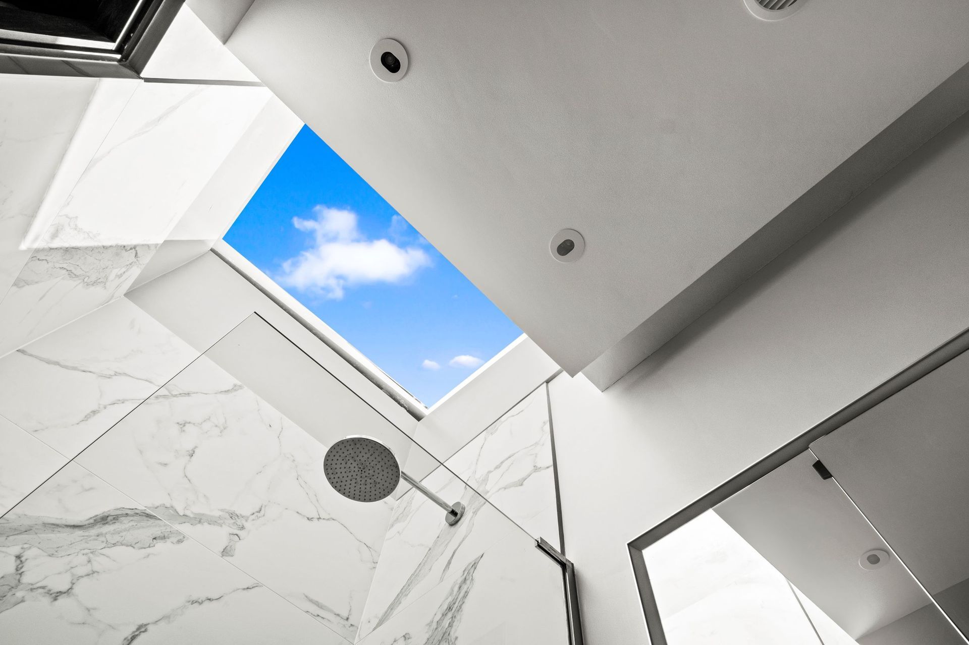 Bathroom with marble walls and a skylight showing a blue sky with clouds.