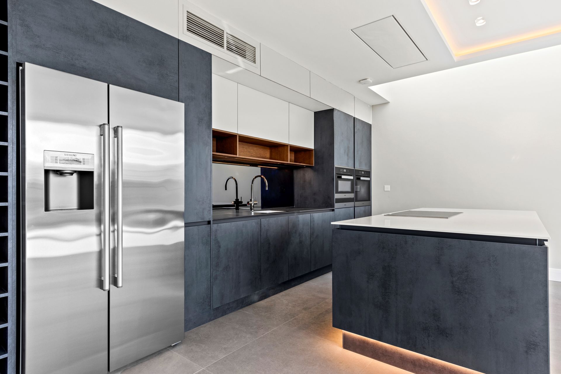 Modern kitchen with stainless steel refrigerator, dark blue cabinetry, white countertops, and an island.