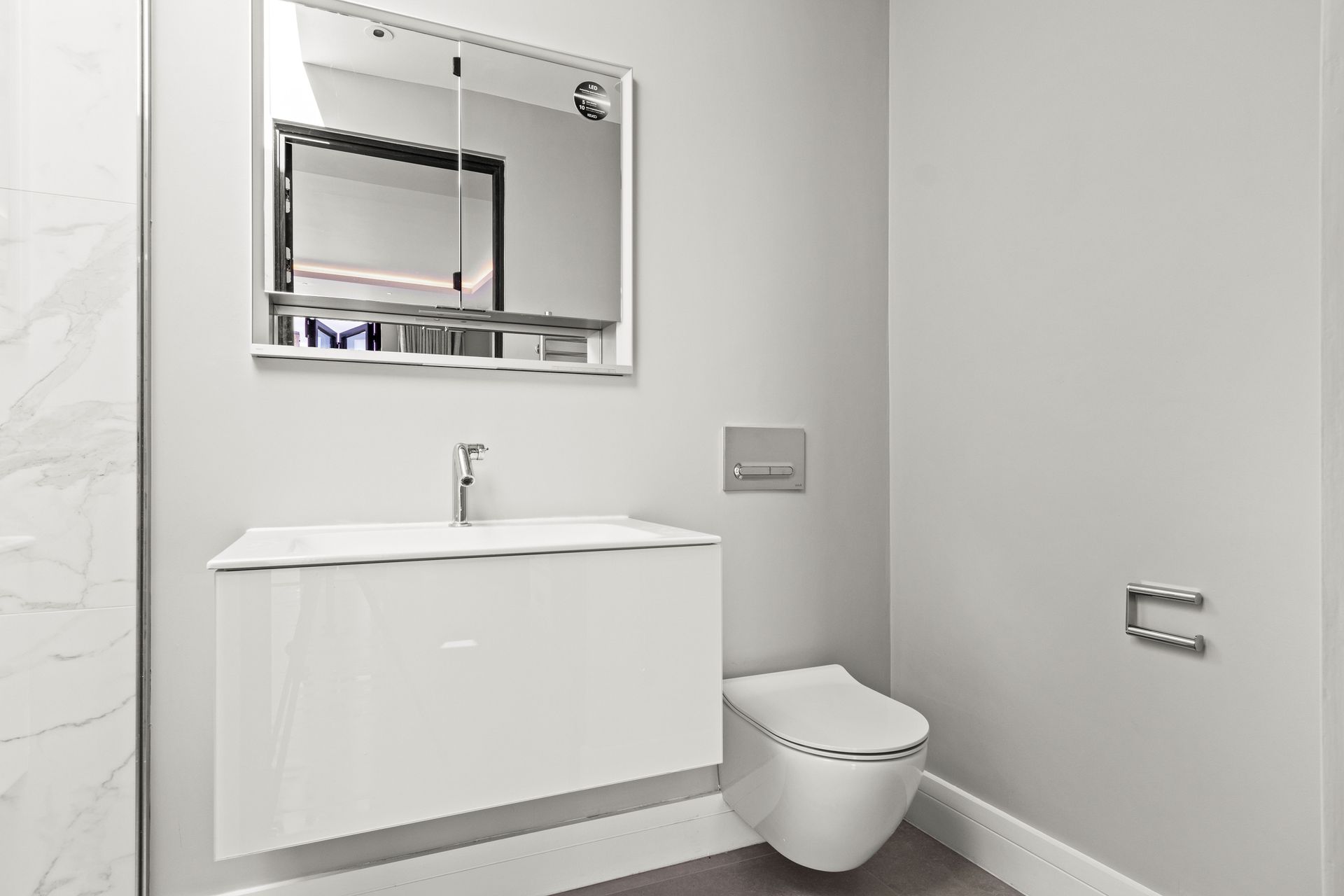Modern, white bathroom with a floating vanity, toilet, and mirrored medicine cabinet.
