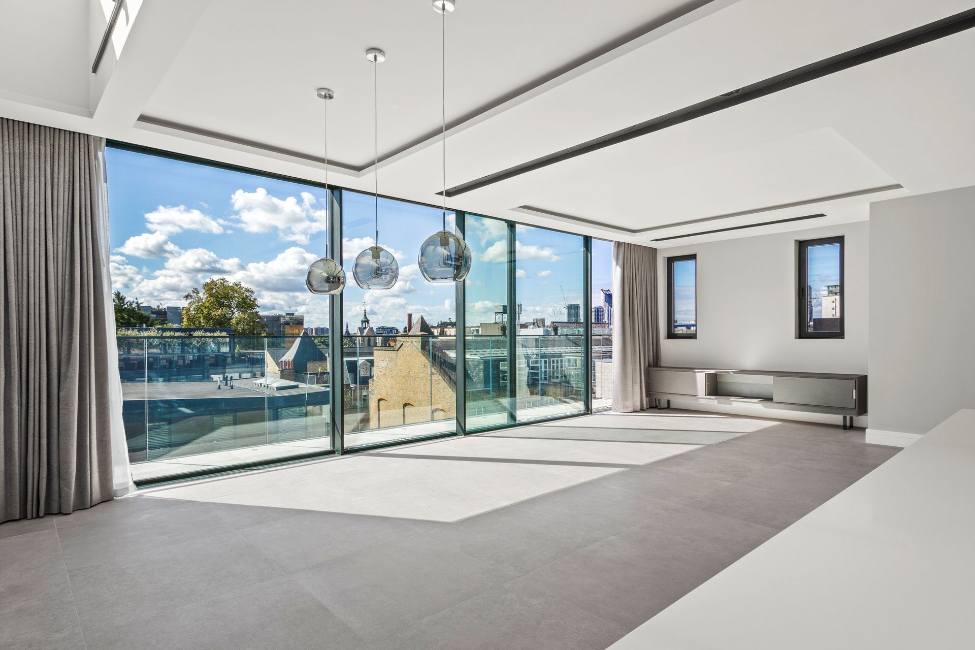 Bright modern living room with large windows, city view, gray curtains, and three hanging lights.