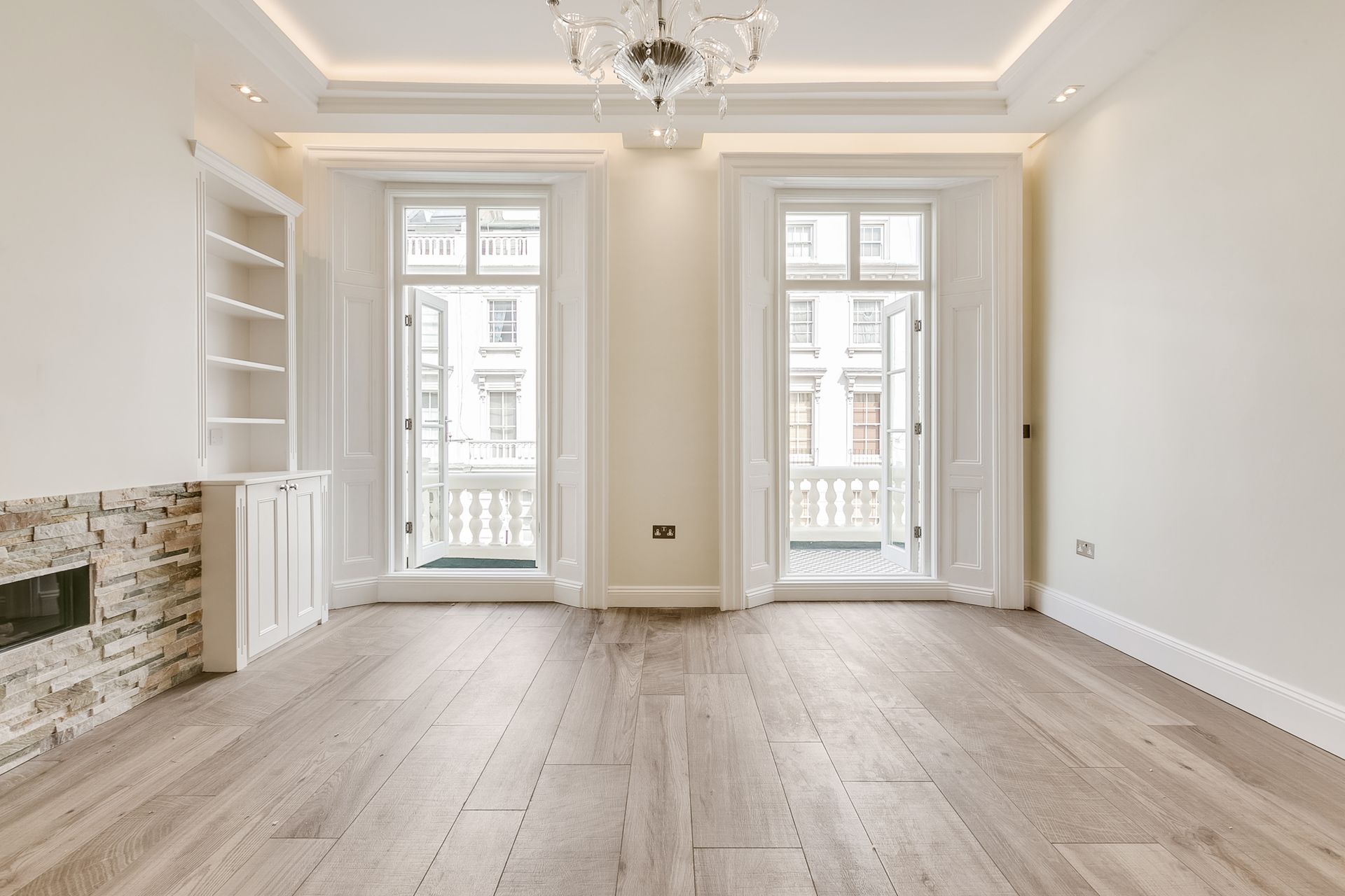 Empty living room with wood floors, two balcony doors, built-in shelving, and a fireplace.