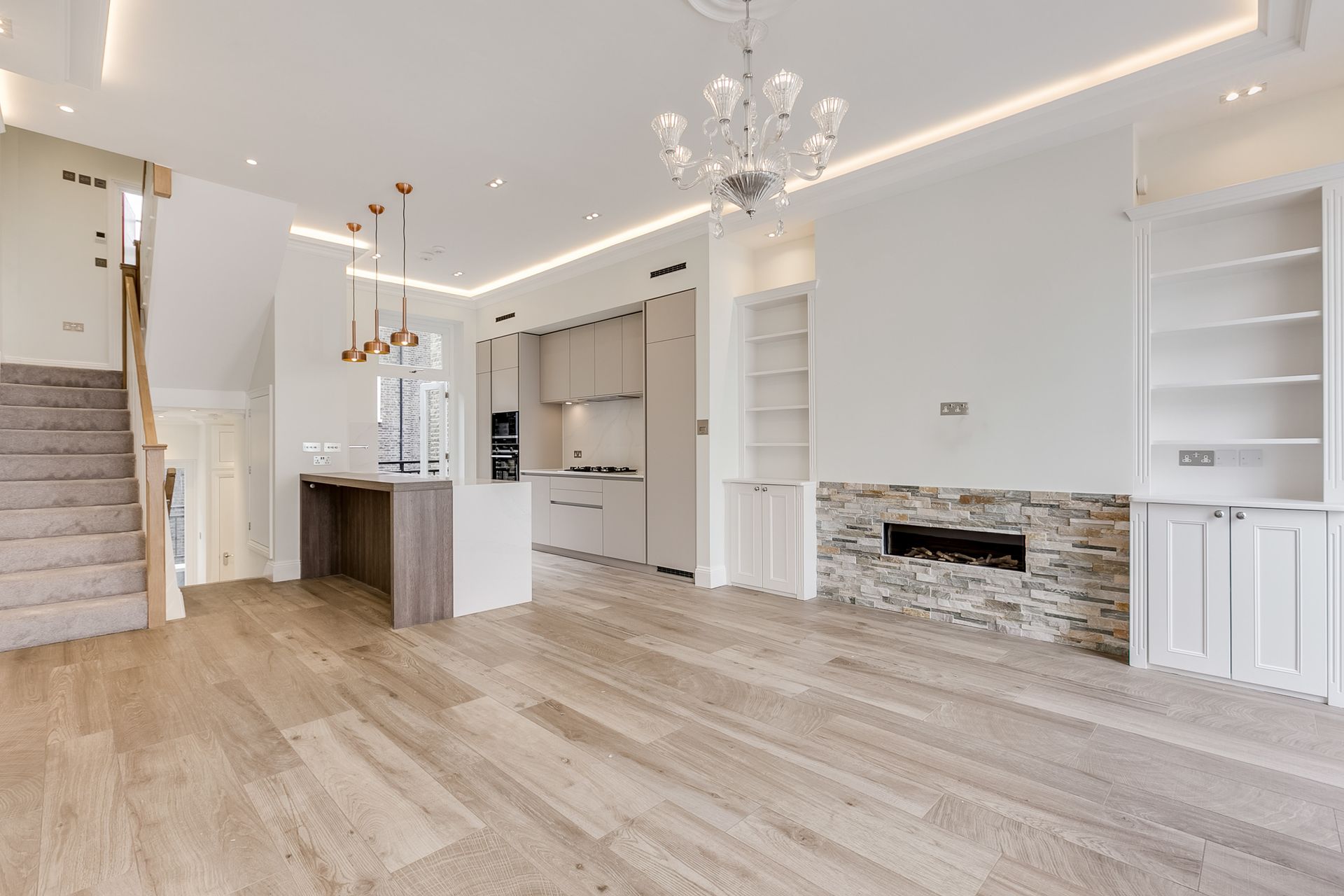 Modern open-plan living space with light wood floors, a kitchen, staircase, and fireplace.