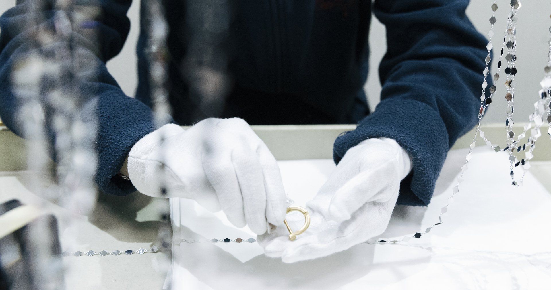 Persona che indossa guanti bianchi esamina un anello d'oro in una gioielleria.