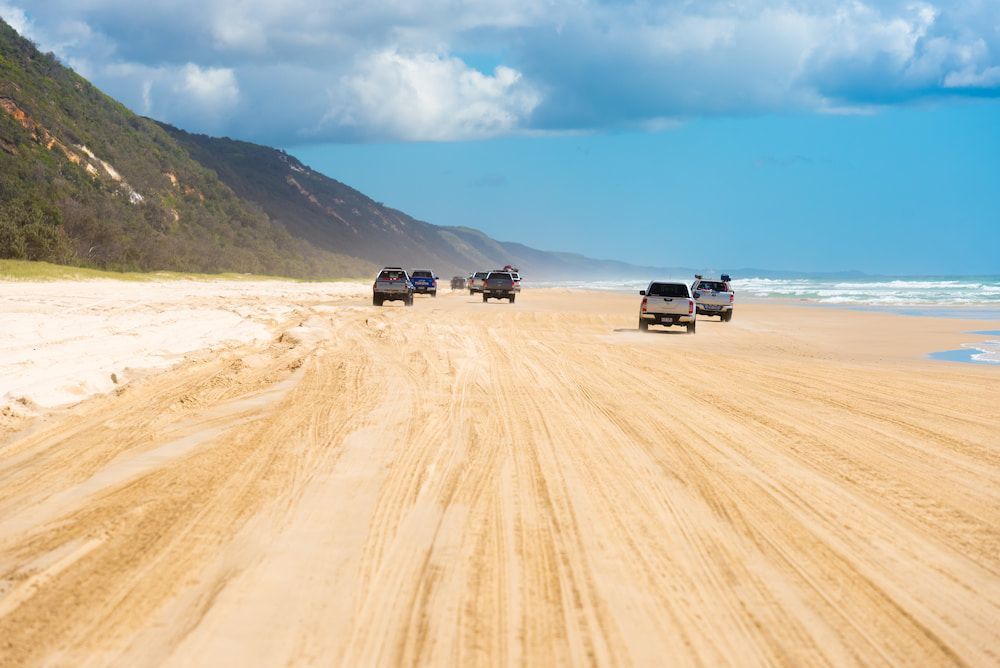 A Group Of Cars Are Driving Down A Dirt Road On A Beach — Rainbow Beach Auto Electrics In Rainbow Beach, QLD