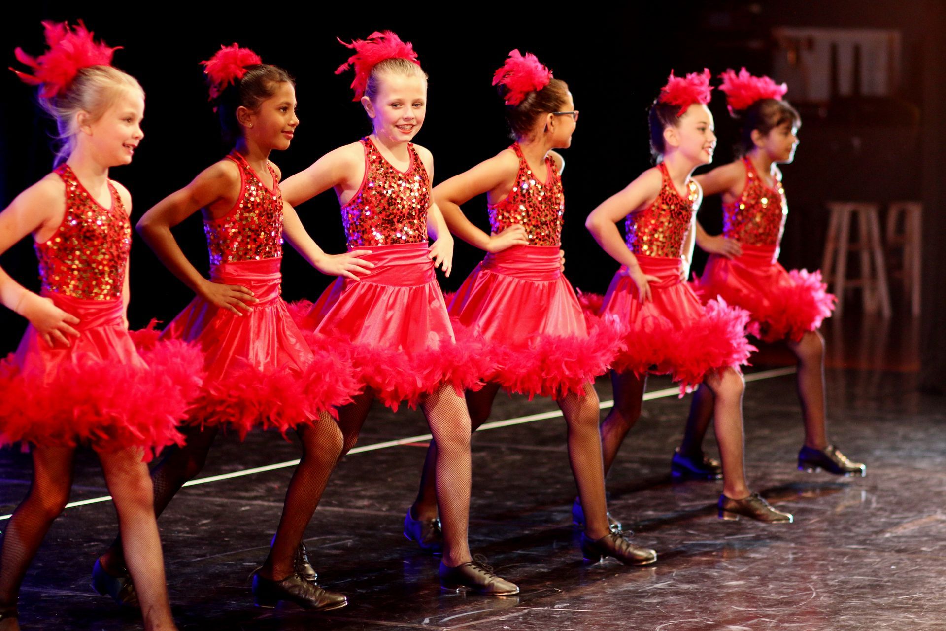 a group of young girls in red tutus are dancing on a stage .