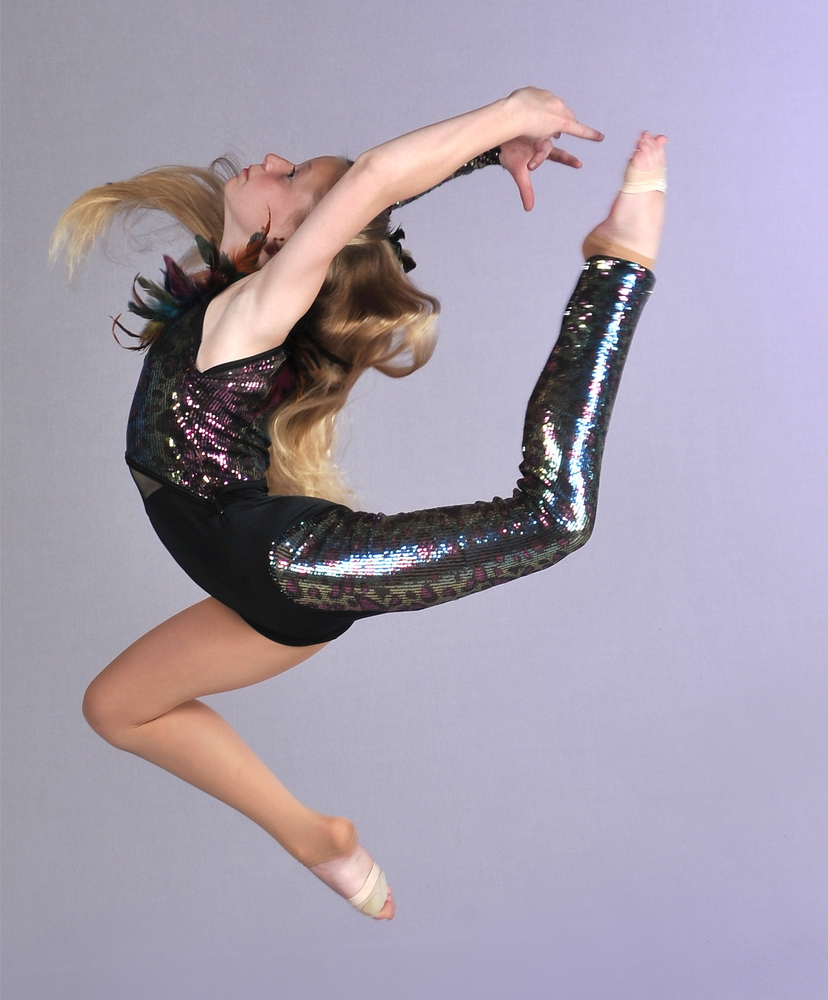 a young girl in a black leotard and sequined pants is jumping in the air