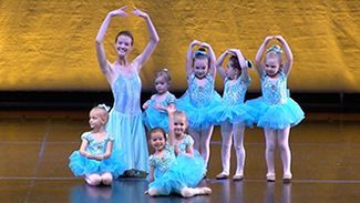 a group of young ballerinas are dancing on a stage .