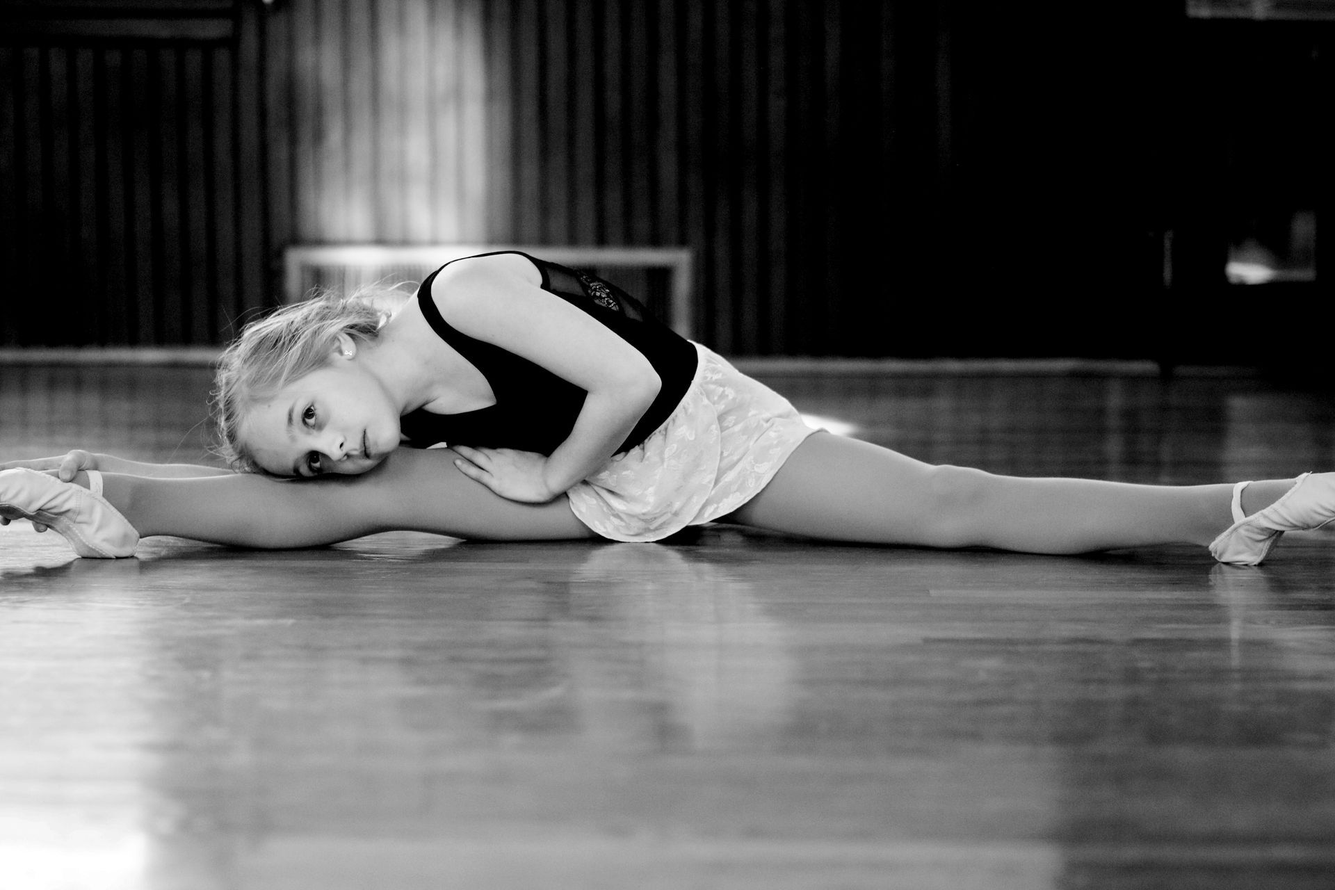 a young ballerina is doing a split on the floor in a black and white photo .