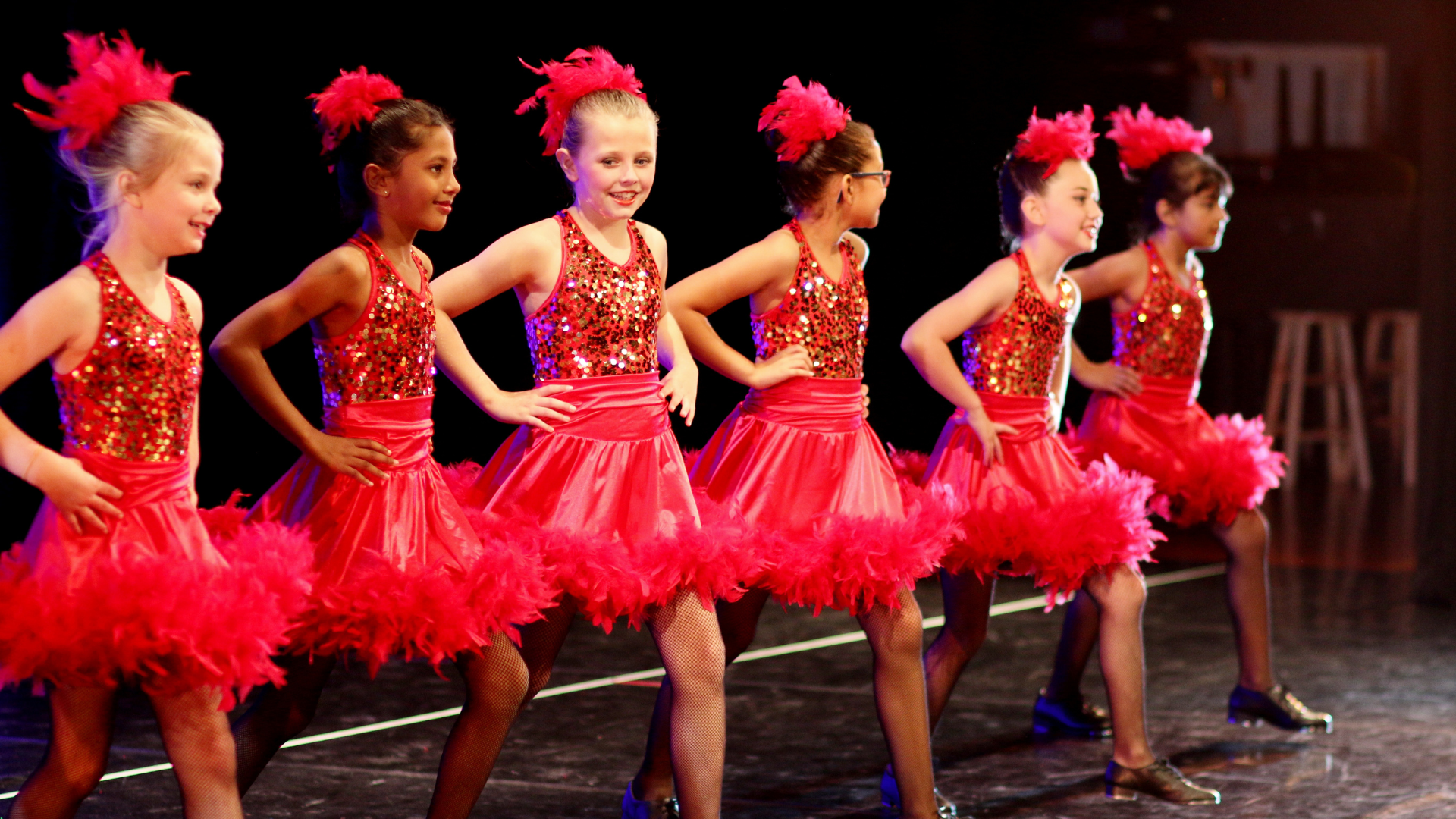 a group of young girls in red dresses are dancing on a stage .