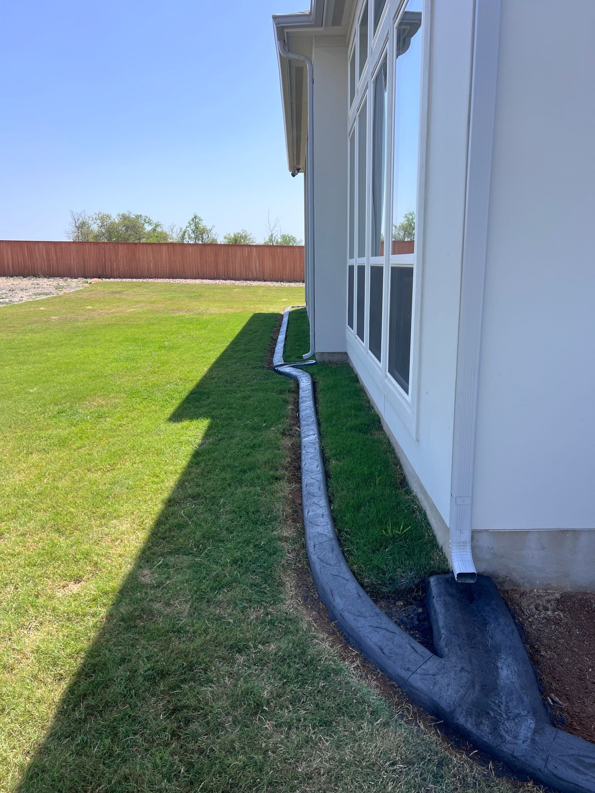 The side of a house with a drain pipe in the grass.