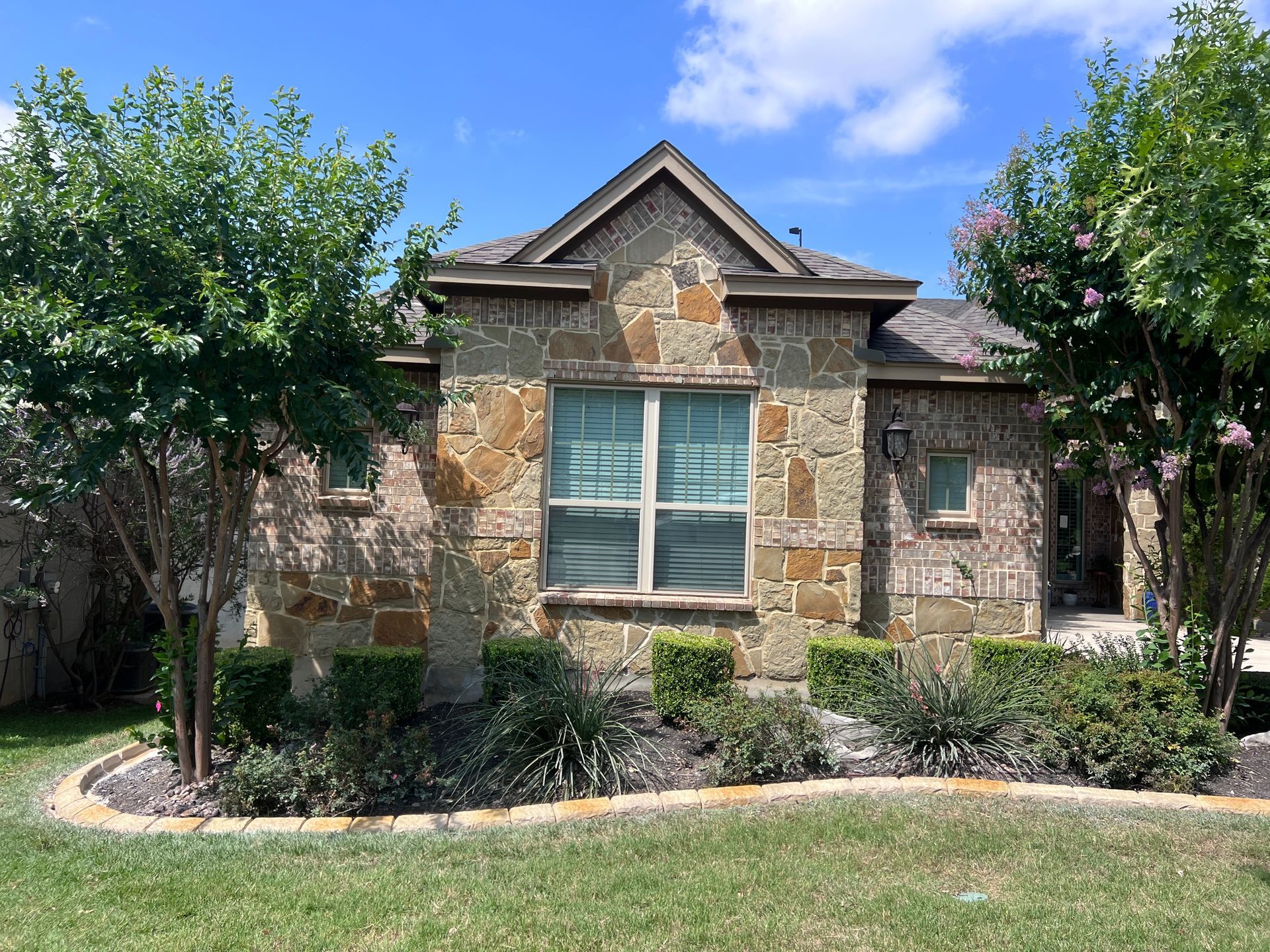 A stone house with a lush green yard and trees in front of it.