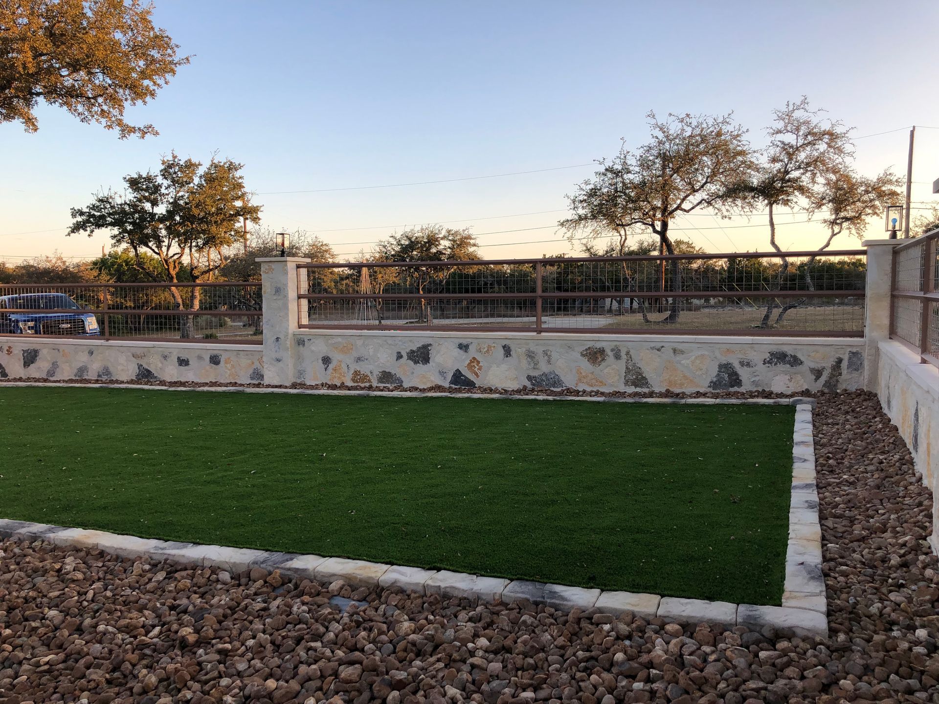 A grassy area with a stone wall and a fence in the background.