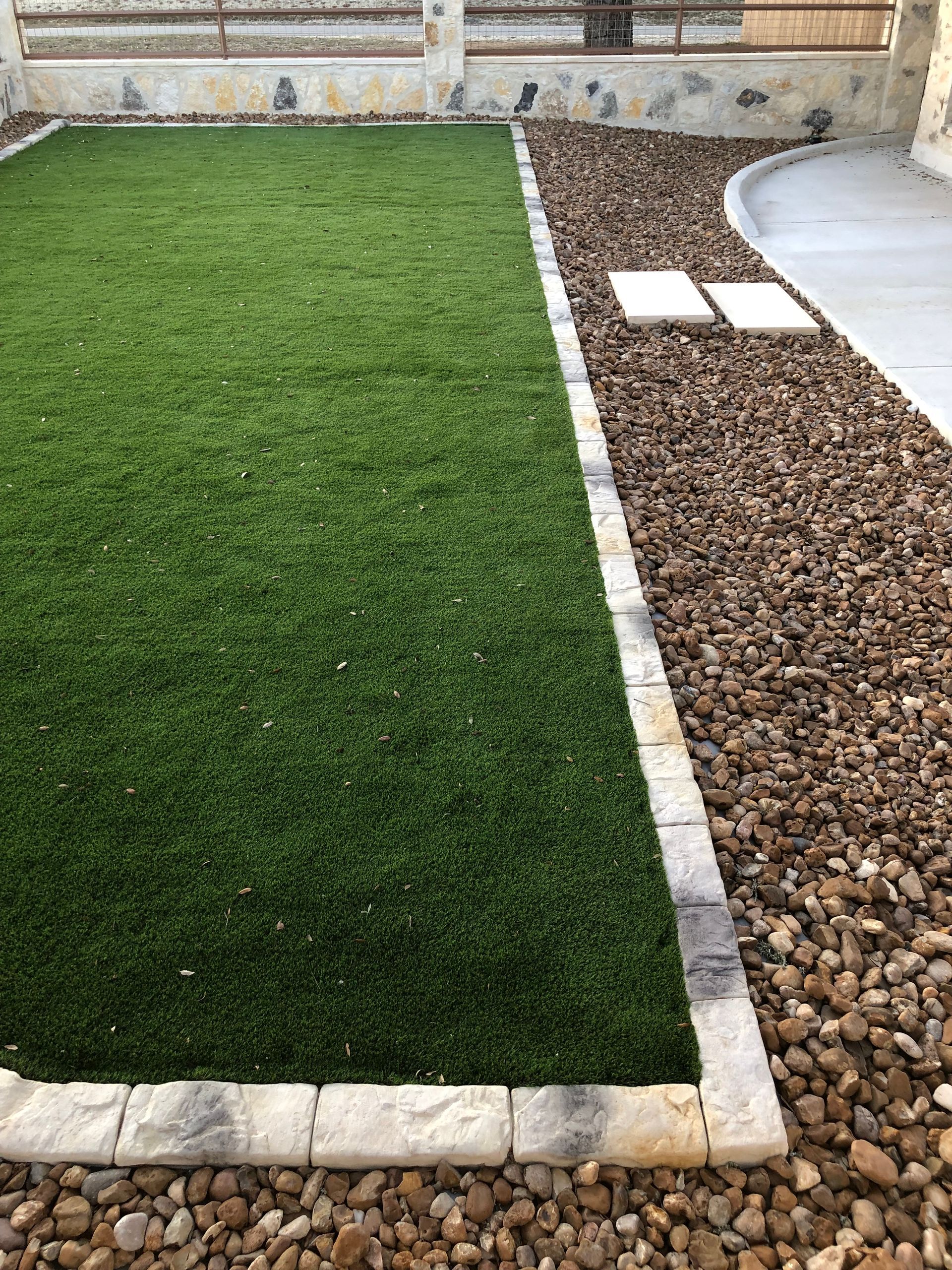 A lawn with a border of rocks and grass in a backyard.