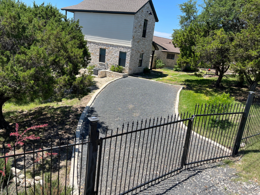 A fence surrounds a driveway leading to a house.