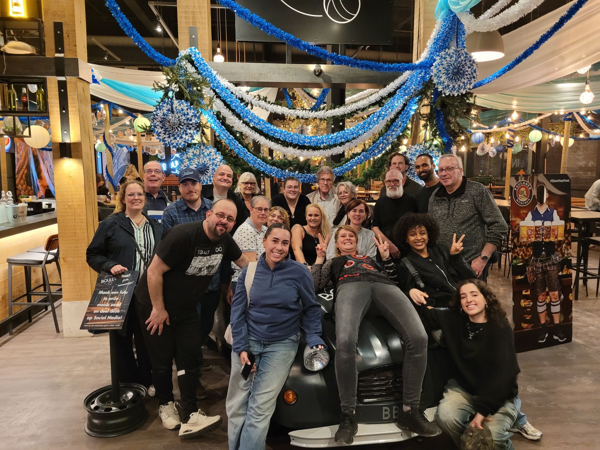 Een groep poseert in een feestelijke binnenruimte met blauwe slingers, kerstbomen en sfeervolle kerstverlichting.