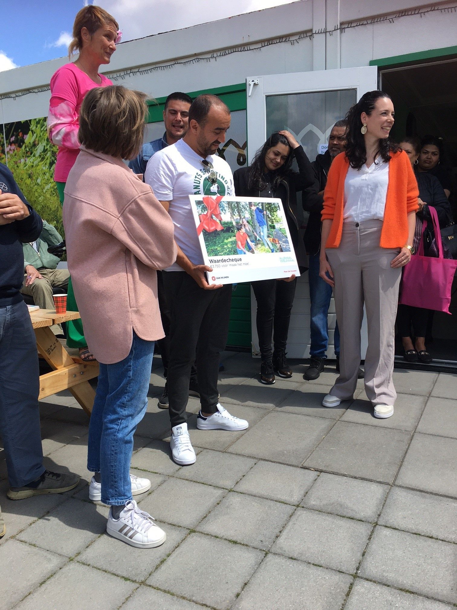 Een groep mensen houdt buiten een kleurrijke poster vast tijdens een bijeenkomst voor een gebouw.