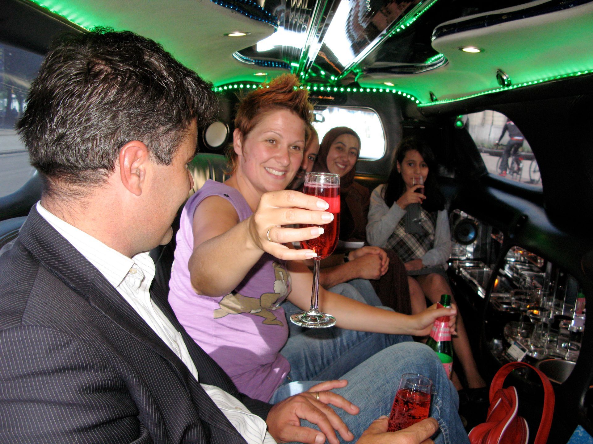 Mensen heffen hun glas in een limousine met neonverlichting, lachend en feestvierend.