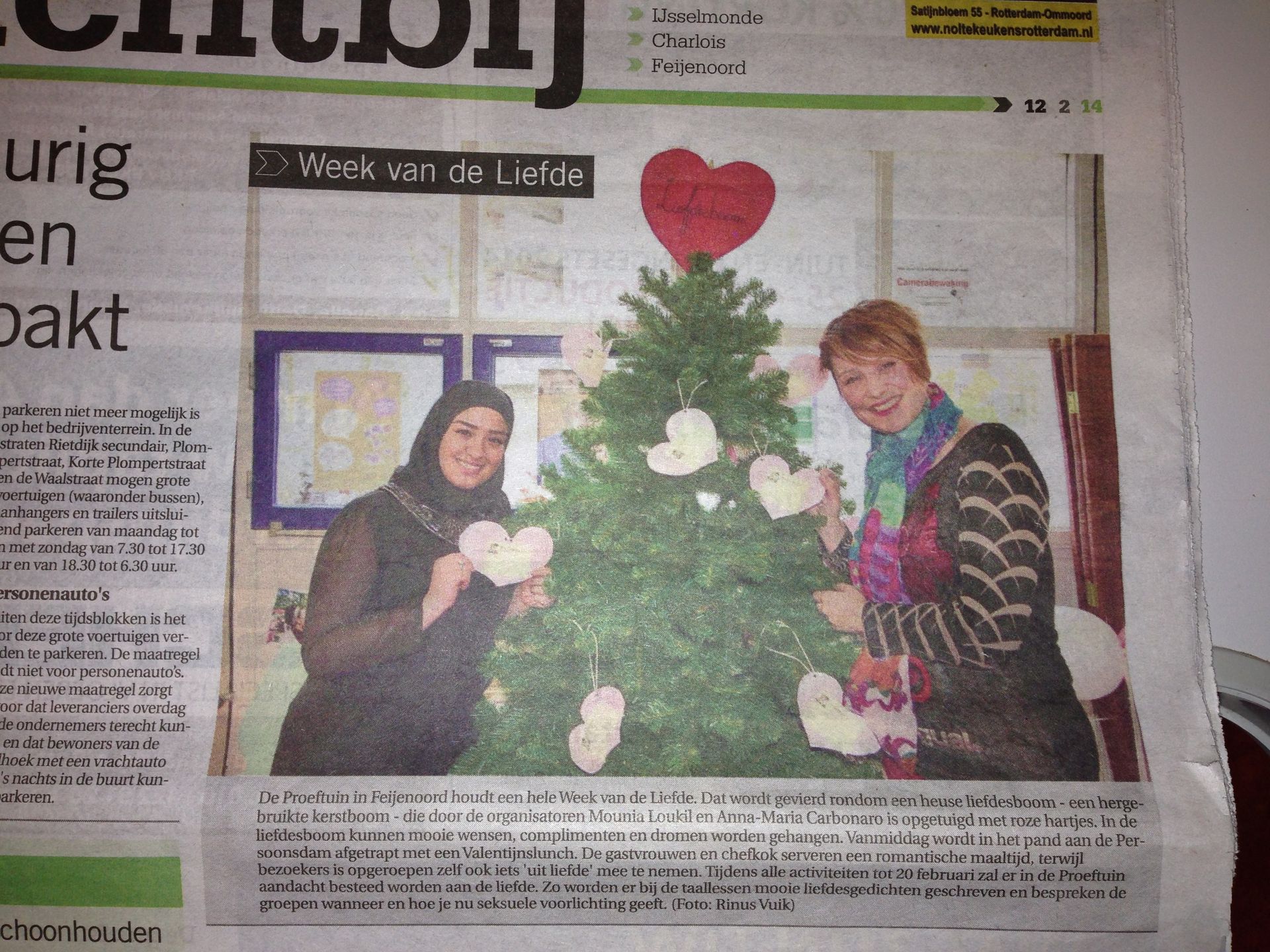 Twee mensen poseren naast een versierde kerstboom met een rood hart als piek.