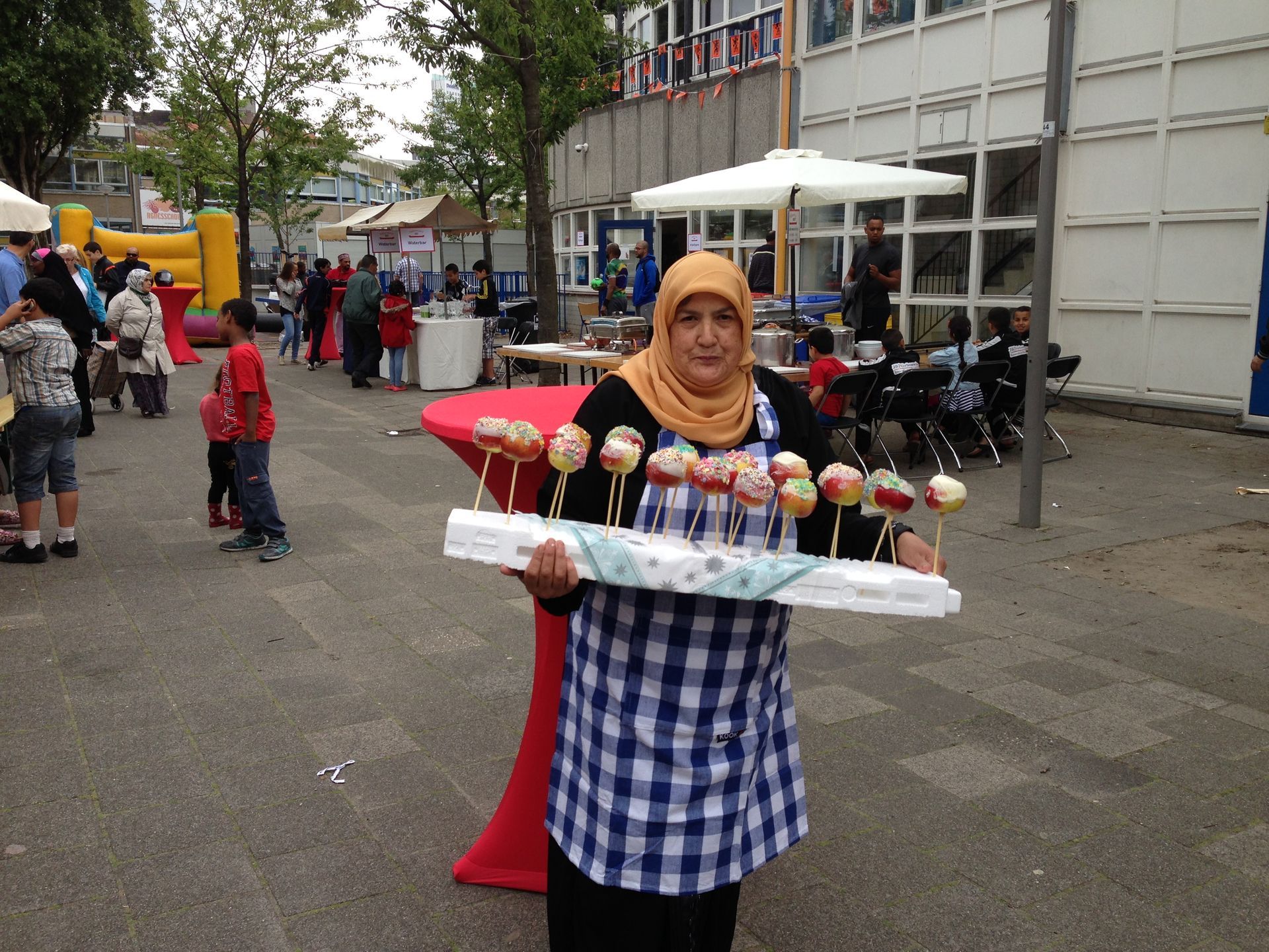 Vrouw met hoofddoek draagt ​​een dienblad met kleurrijke ijshoorntjes op een openluchtmarkt.