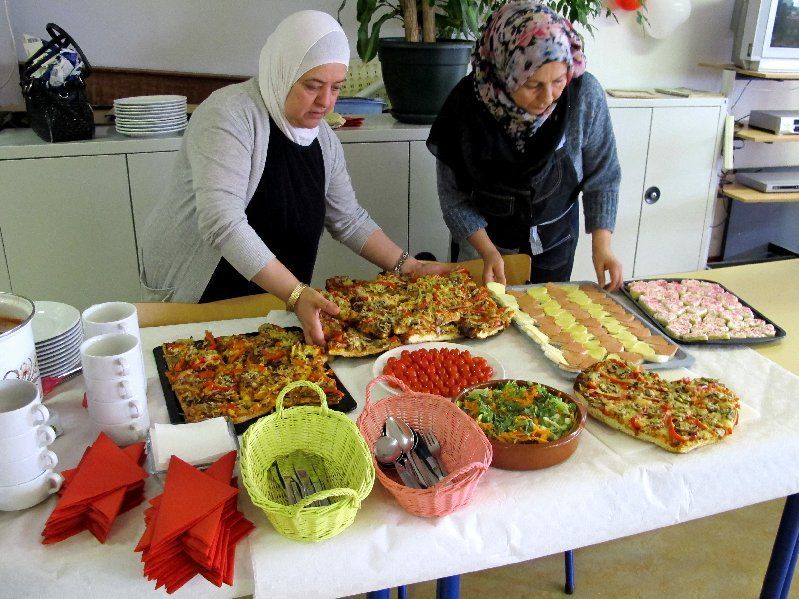 Twee vrouwen bereiden diverse gerechten op een tafel in een keukenomgeving.
