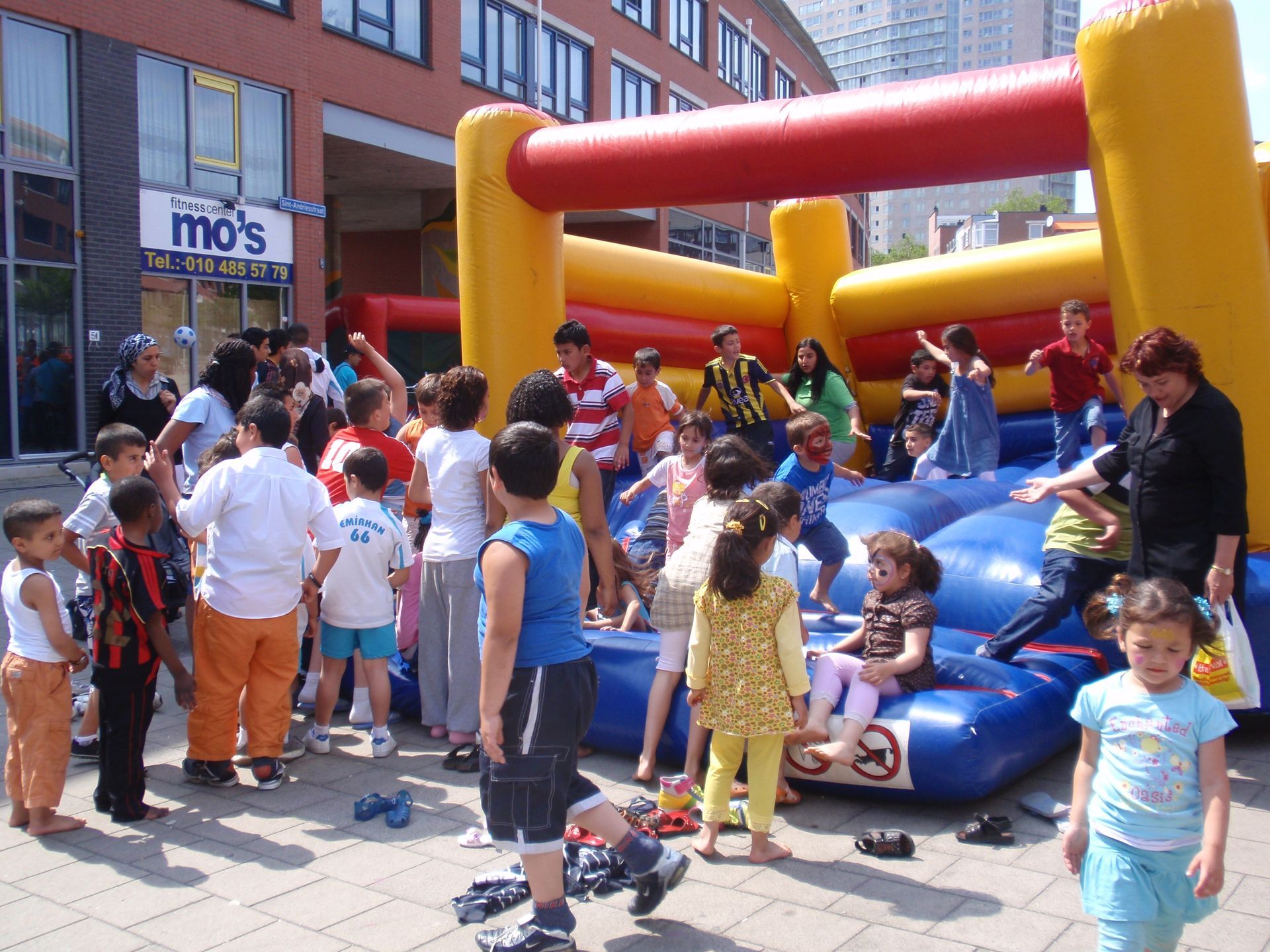 Mensen verzamelden zich rond een blauwe opblaasbare speelstructuur tijdens een evenement in de openlucht.