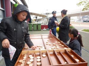 Mensen spelen een houten bordspel aan een kraam op een buitenmarkt.