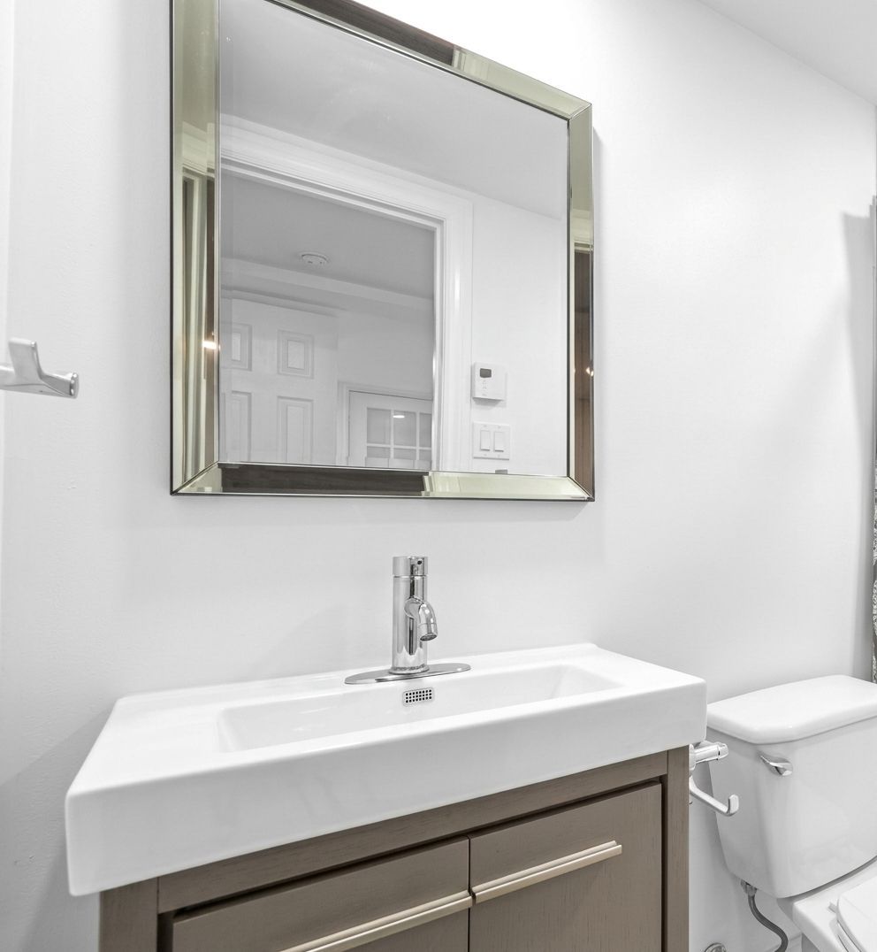 Modern bathroom vanity with rectangular mirror, white sink, and toilet against light gray walls
