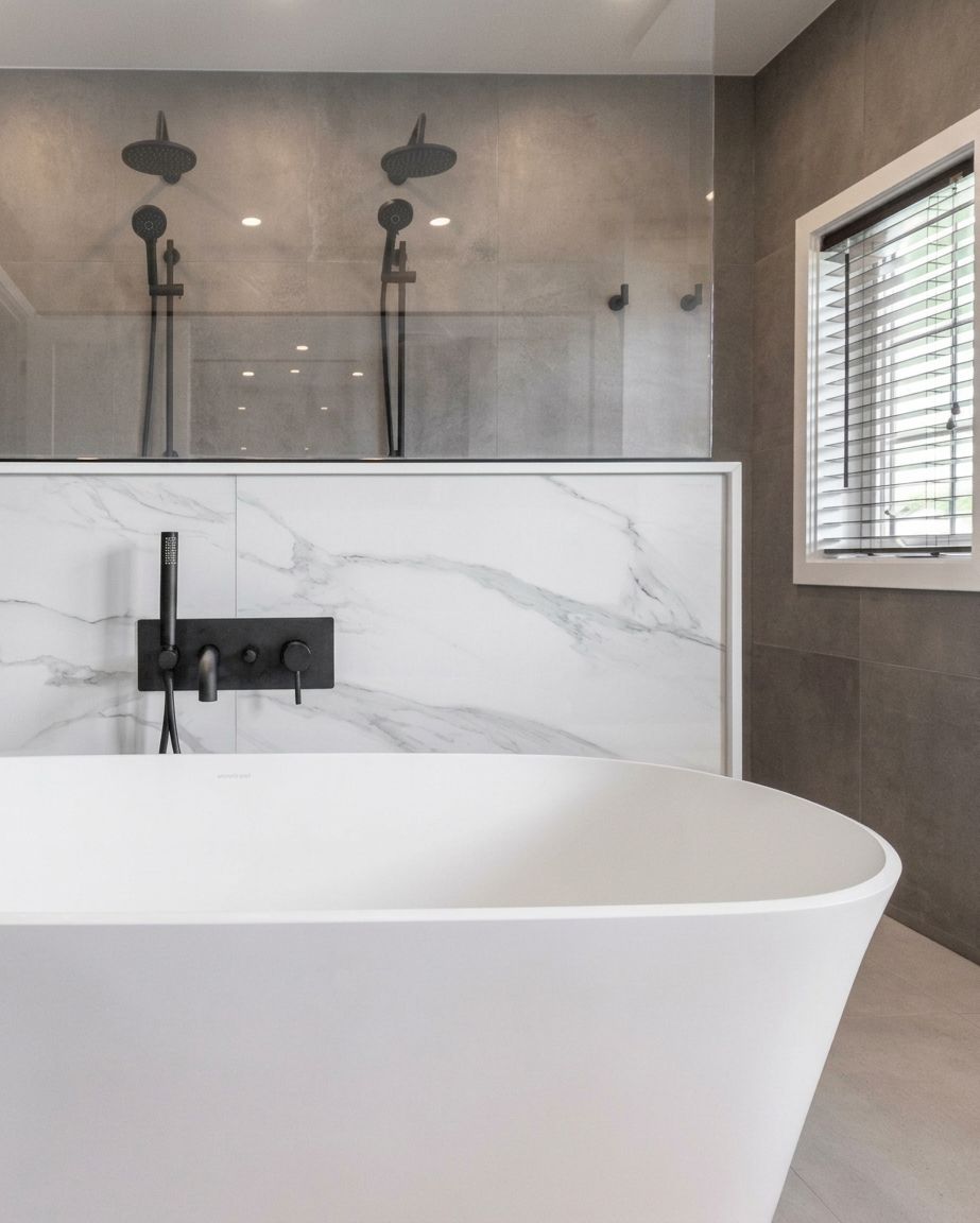 Modern bathroom with white freestanding tub, glass shower, marble wall, and black fixtures