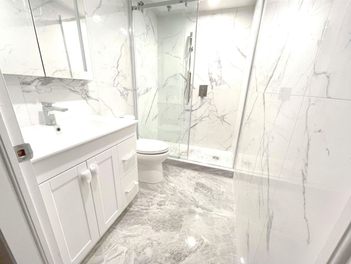 Bright marble bathroom with white vanity, sink, toilet, and glass shower enclosure.