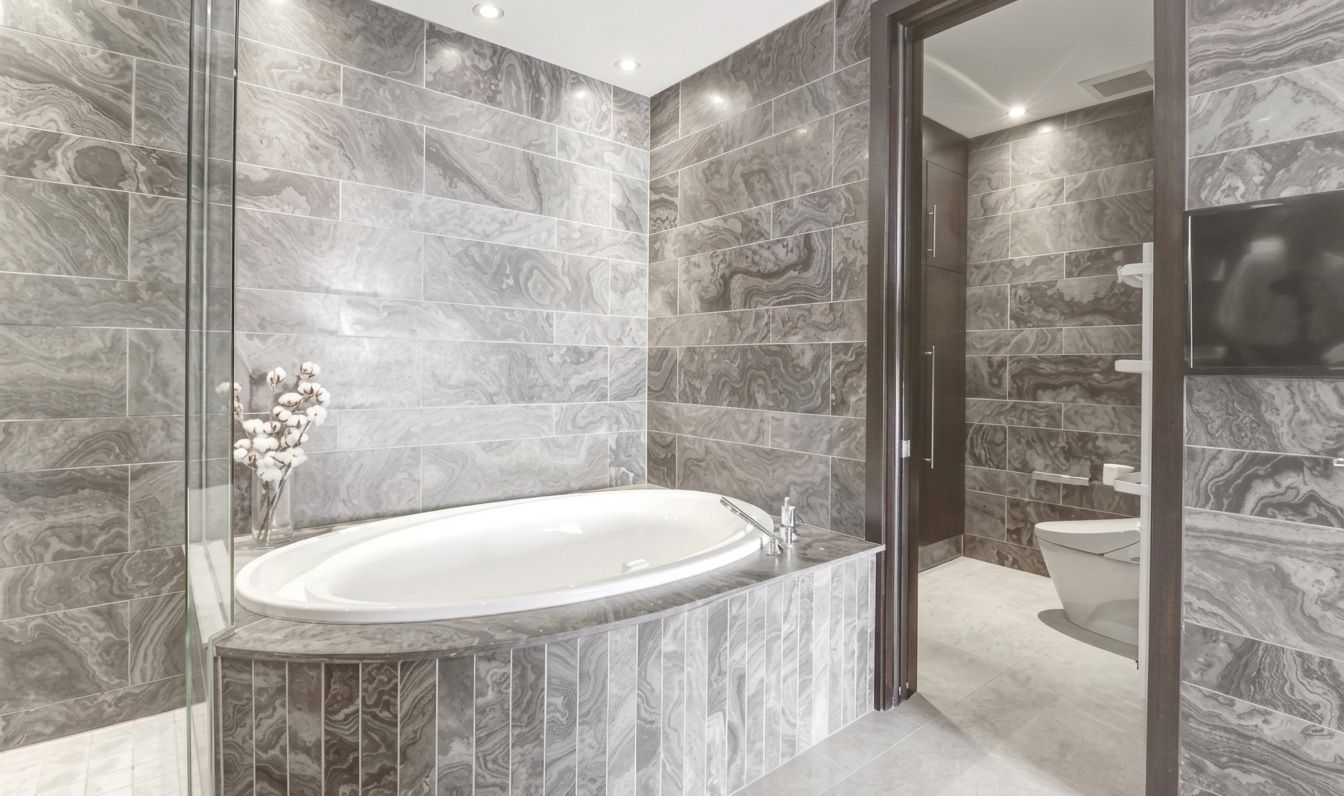 Luxurious gray marble bathroom with a built-in oval soaking tub and glass shower enclosure