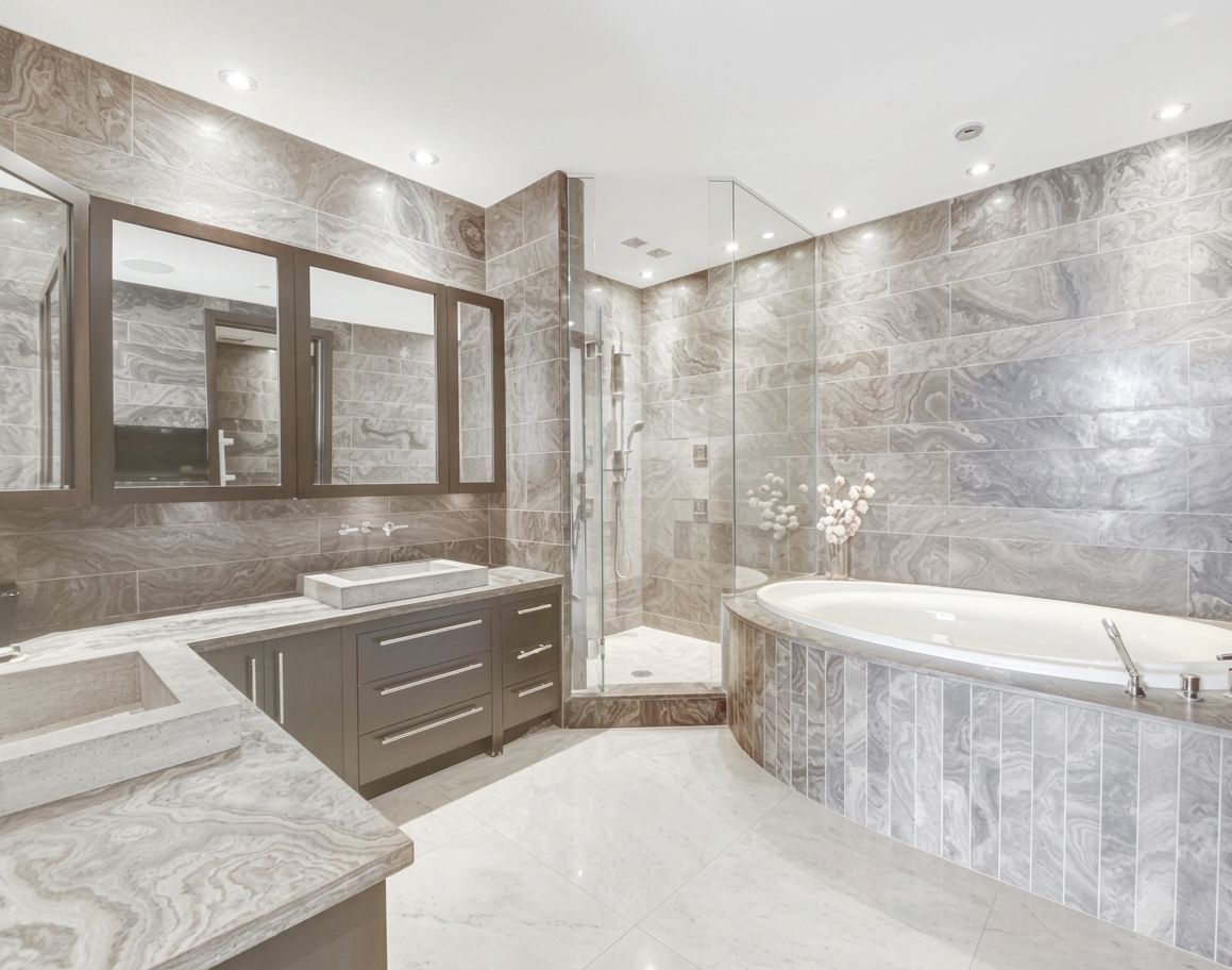 Luxurious bathroom with marble walls, double vanity, large mirror, glass shower, and soaking tub