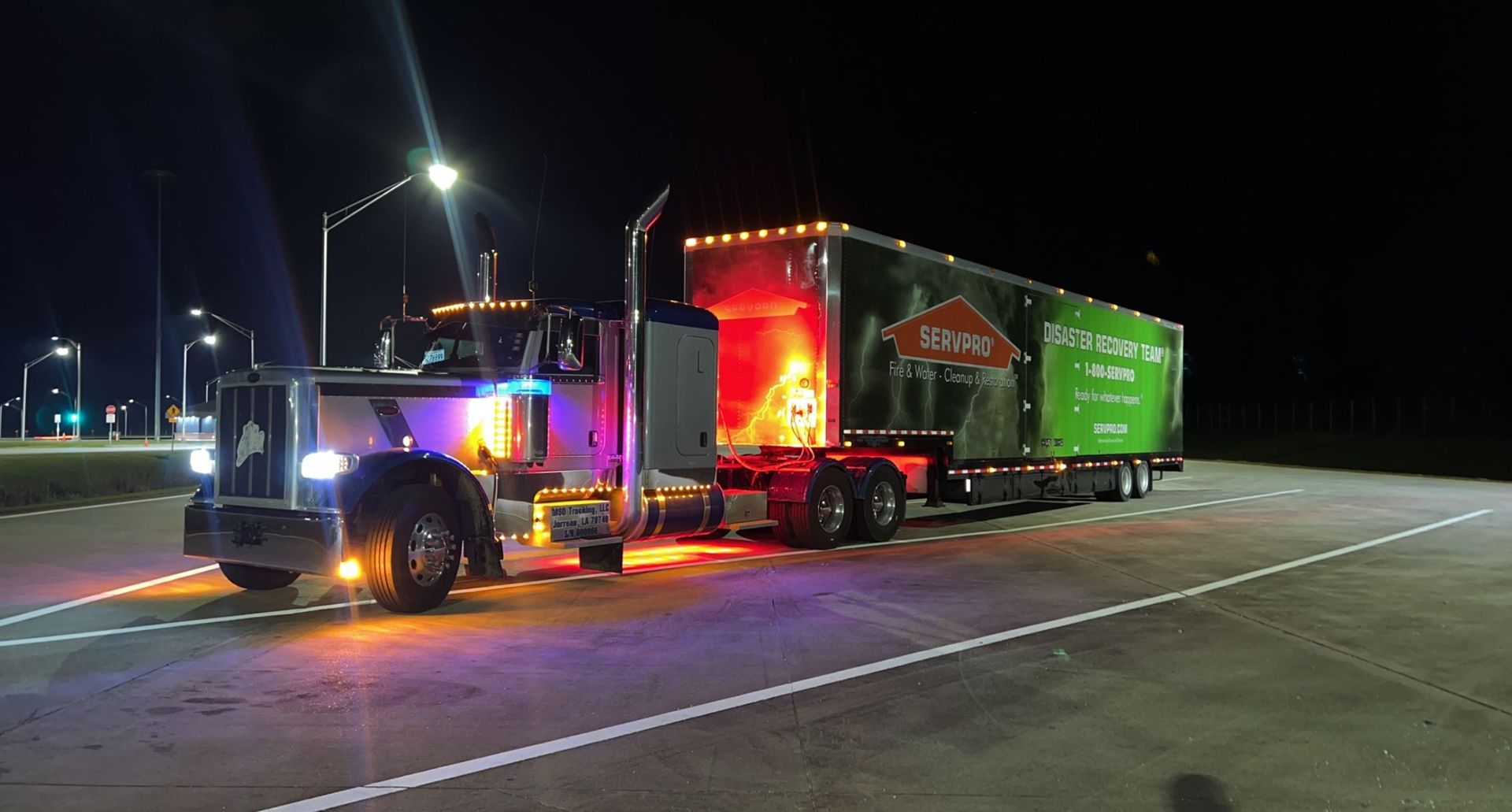 A semi-truck with colorful lights parked at night. Trailer has a green logo.