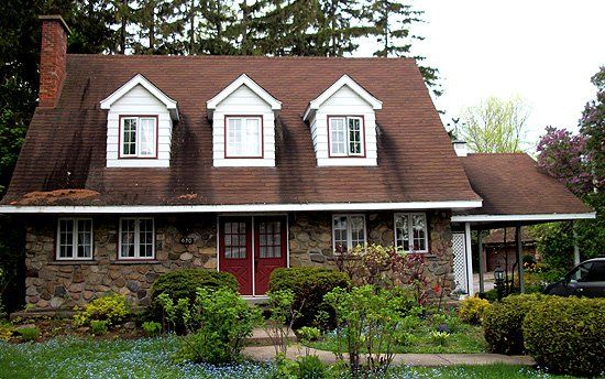 A stone house with a brown roof and white trim
