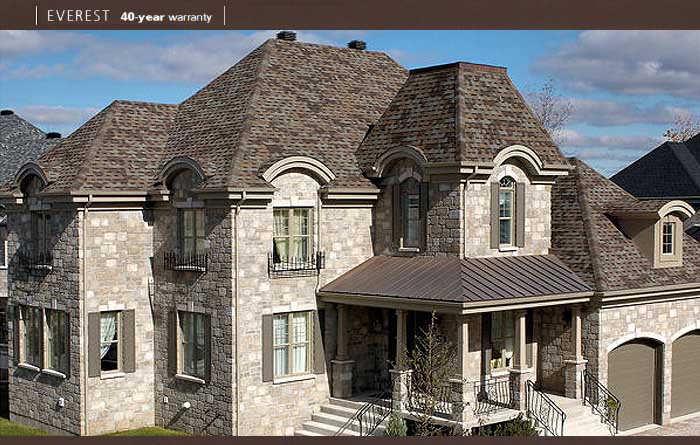 Une grande maison en pierre avec un toit brun et un garage