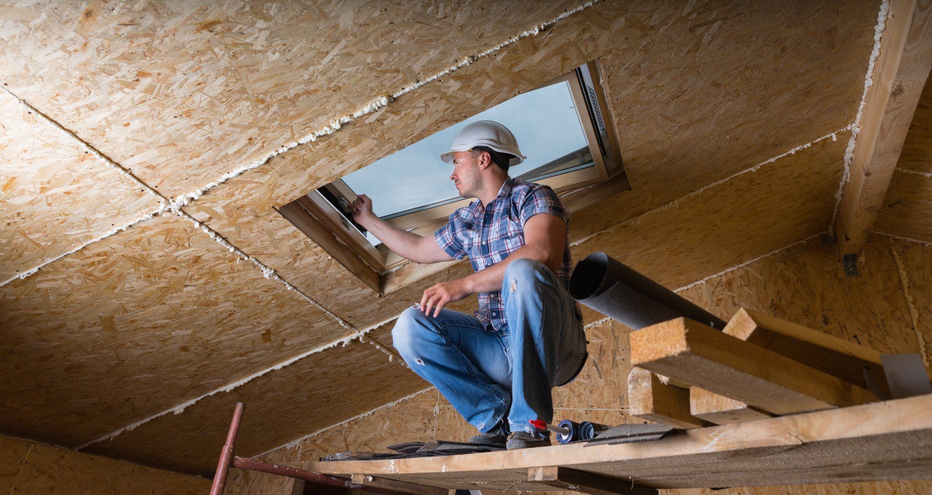 A man is looking out of a skylight in a building under construction.