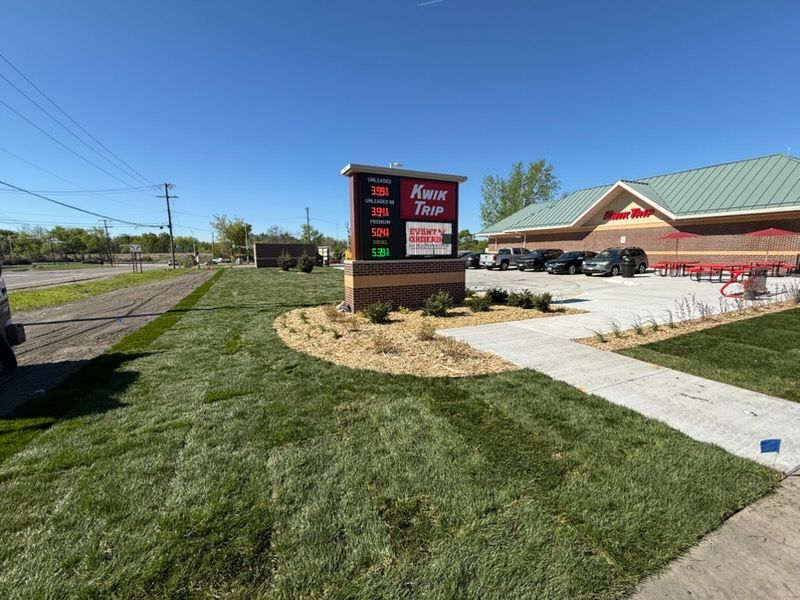 Convenience store with roadside sign, green lawn, and parking lot under a clear blue sky