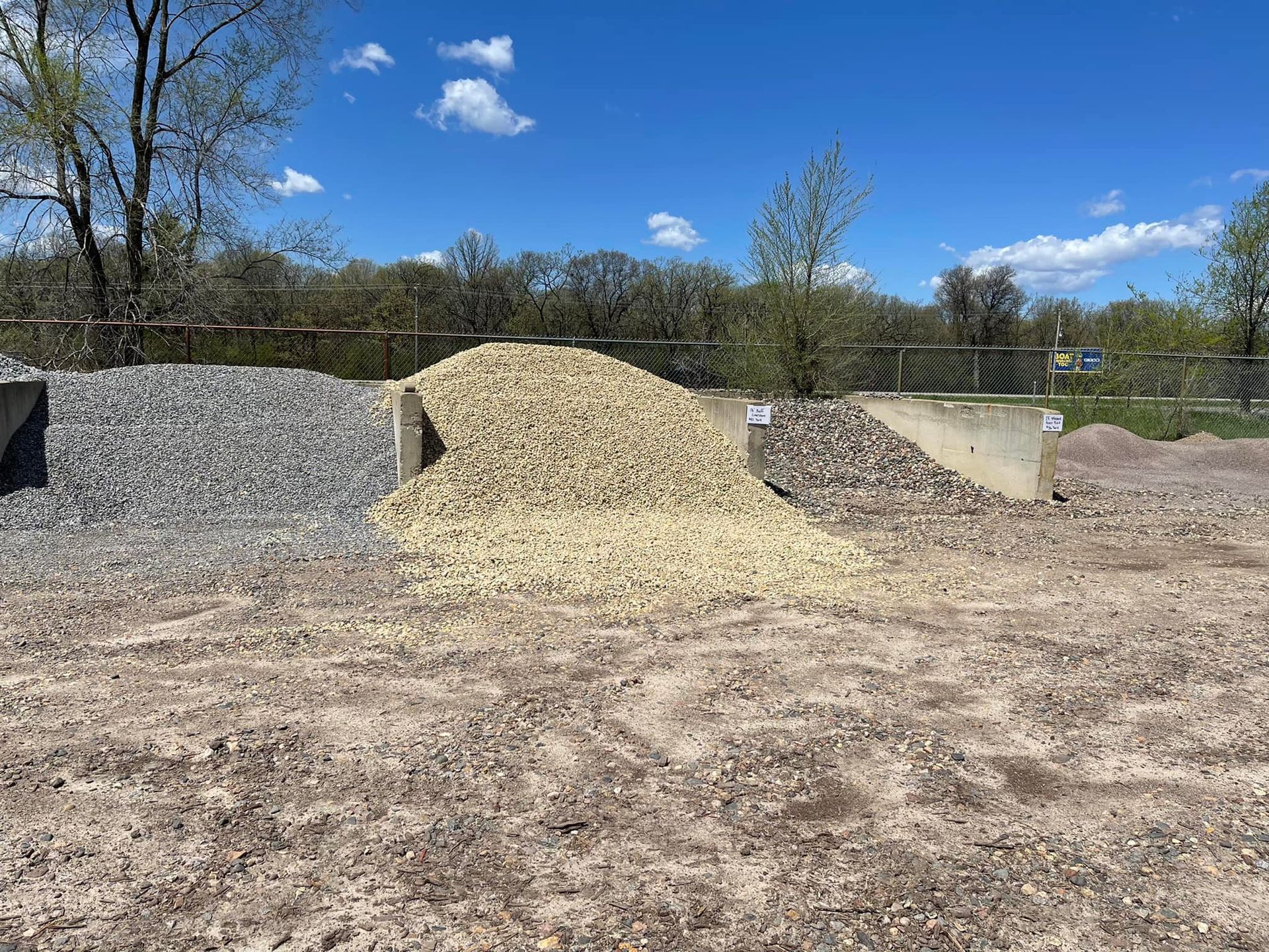 Outdoor gravel piles in gray, tan, and beige under a blue sky in a construction or landscaping yard