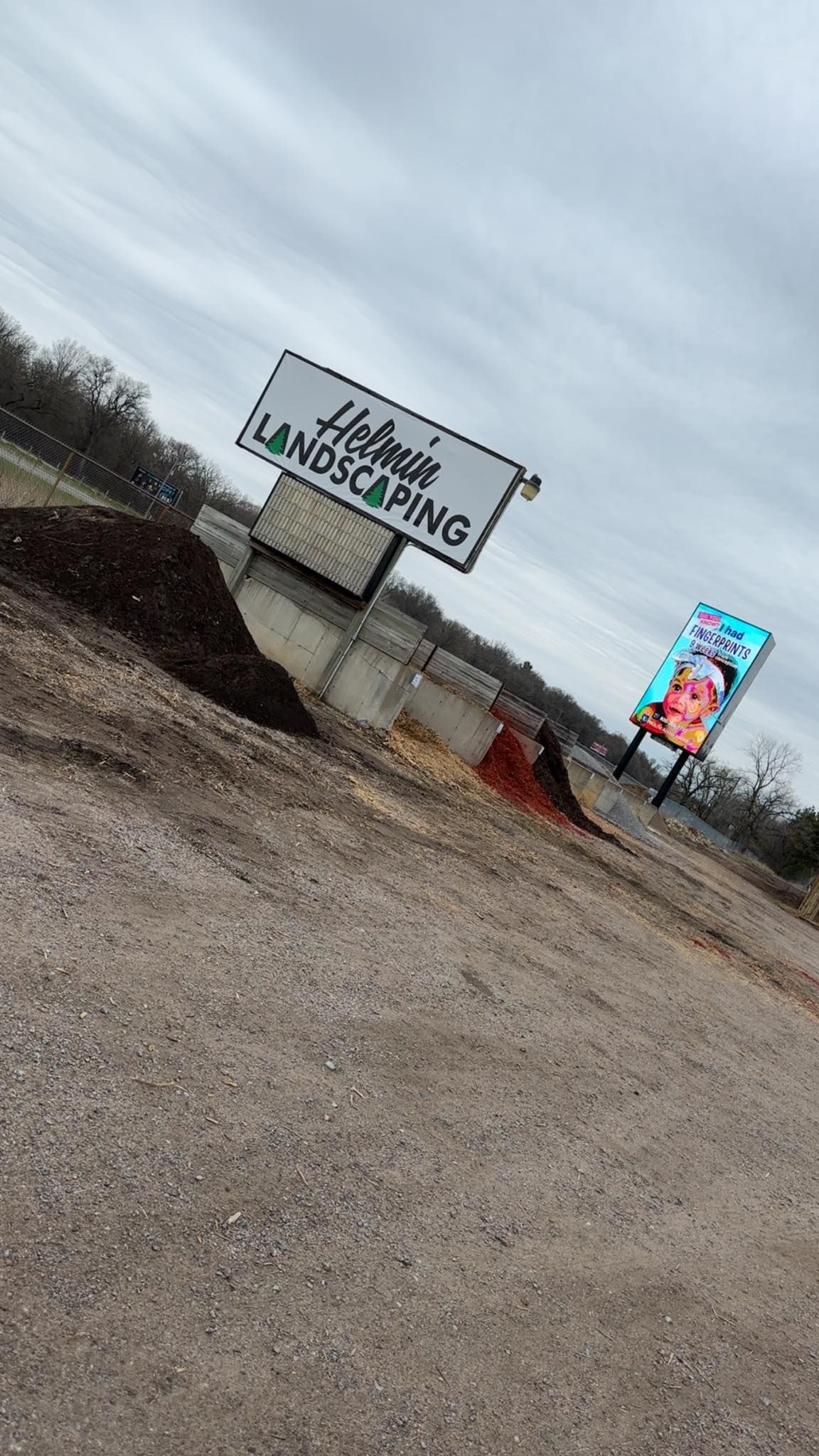 Tilted roadside sign reading “FBI Investigations” by a gravel lot under a cloudy sky