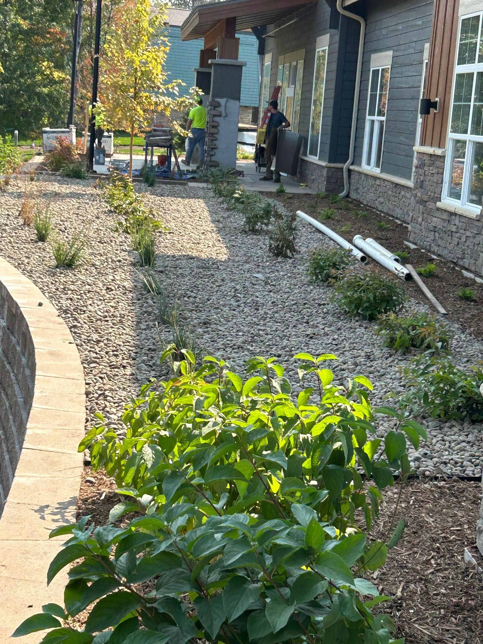 Stone walkway beside a house, with gravel landscaping and green shrubs in the foreground.
