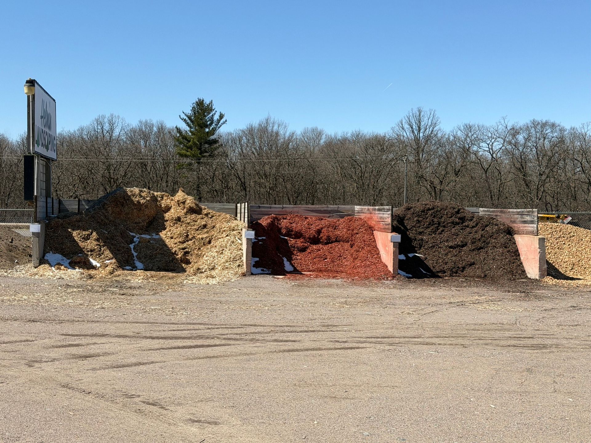 Open gravel lot with large dirt and rock piles, including red and tan sections, under a clear blue sky.