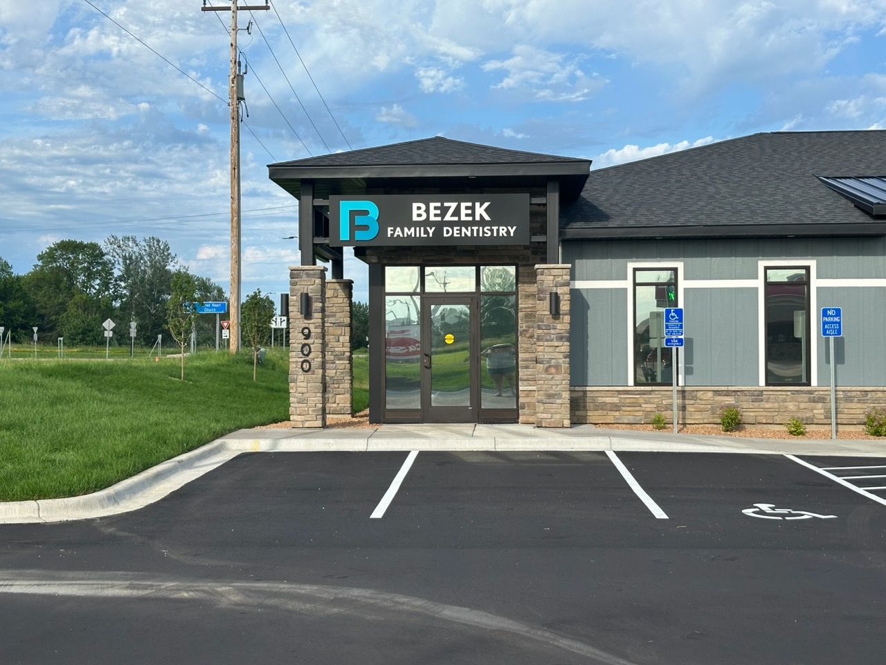 Bezek Family Dentistry storefront with glass entrance and empty parking spaces under a blue sky