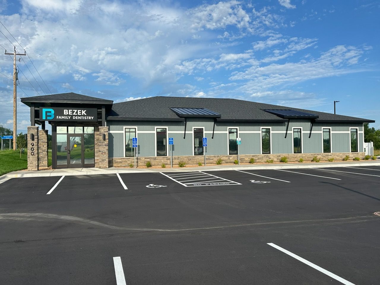 Single-story roadside building with a dark roof, stone entrance, and empty parking lot under a blue sky.