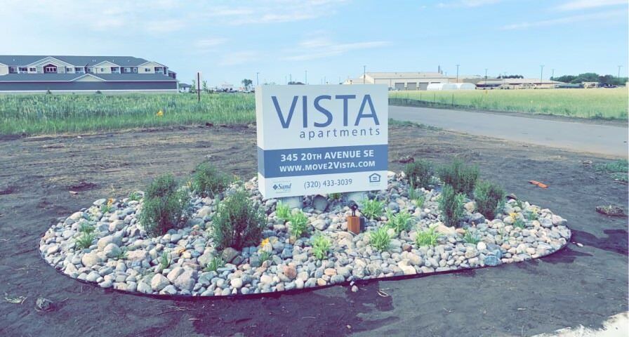 VISTA neighborhood entrance sign in a landscaped rock bed beside a dirt road and open fields
